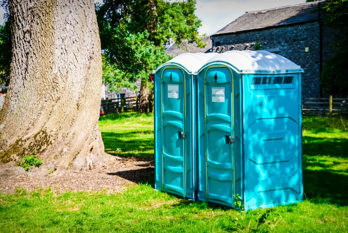 Two blue portable toilets beside a tree at an outdoor event in the UK